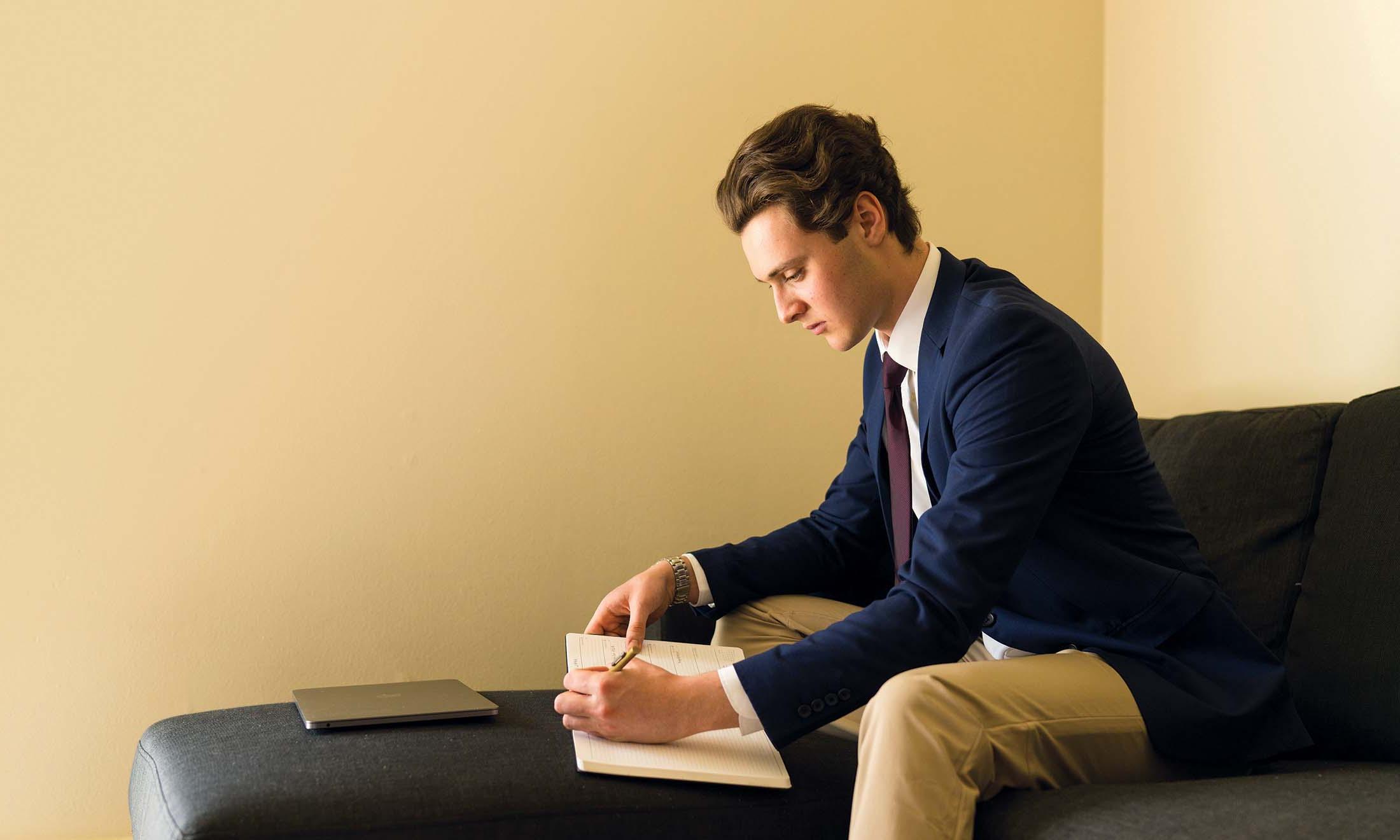 Male student sitting on chair writing in notebook